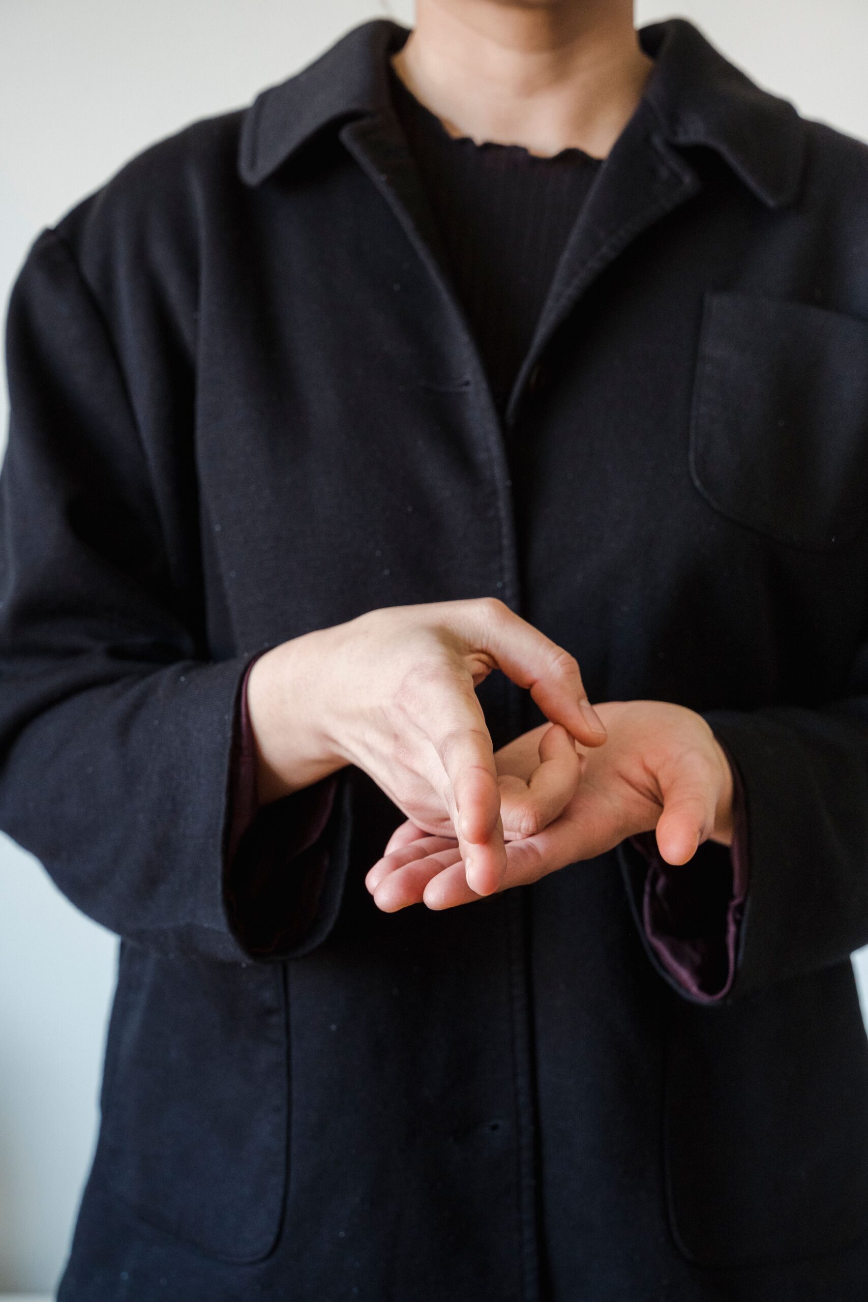 Close-up of a person in a black coat making a gesture with their hands, indoors.
